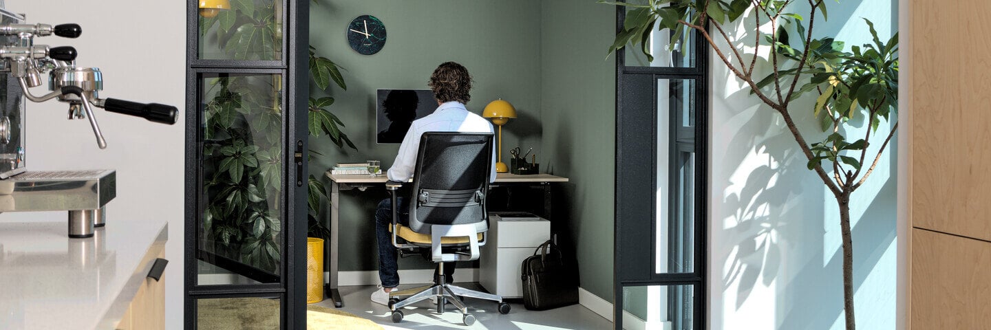 headerxl-Royal-Ahrend-balance-workstation-in-grey-with-oak-tabletop-and-Ease-office-chair-upholstered-in-yellow-and-black-with-male-model-interior-view